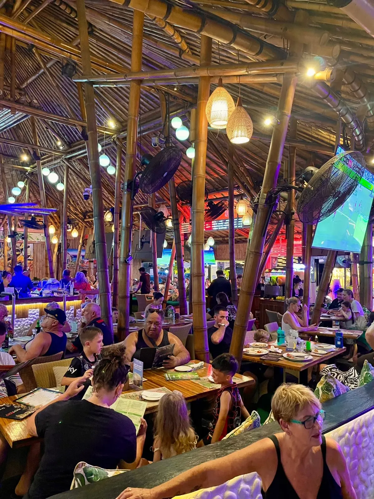 The Bamboo room at night, tables under the thatched roof with the screens on